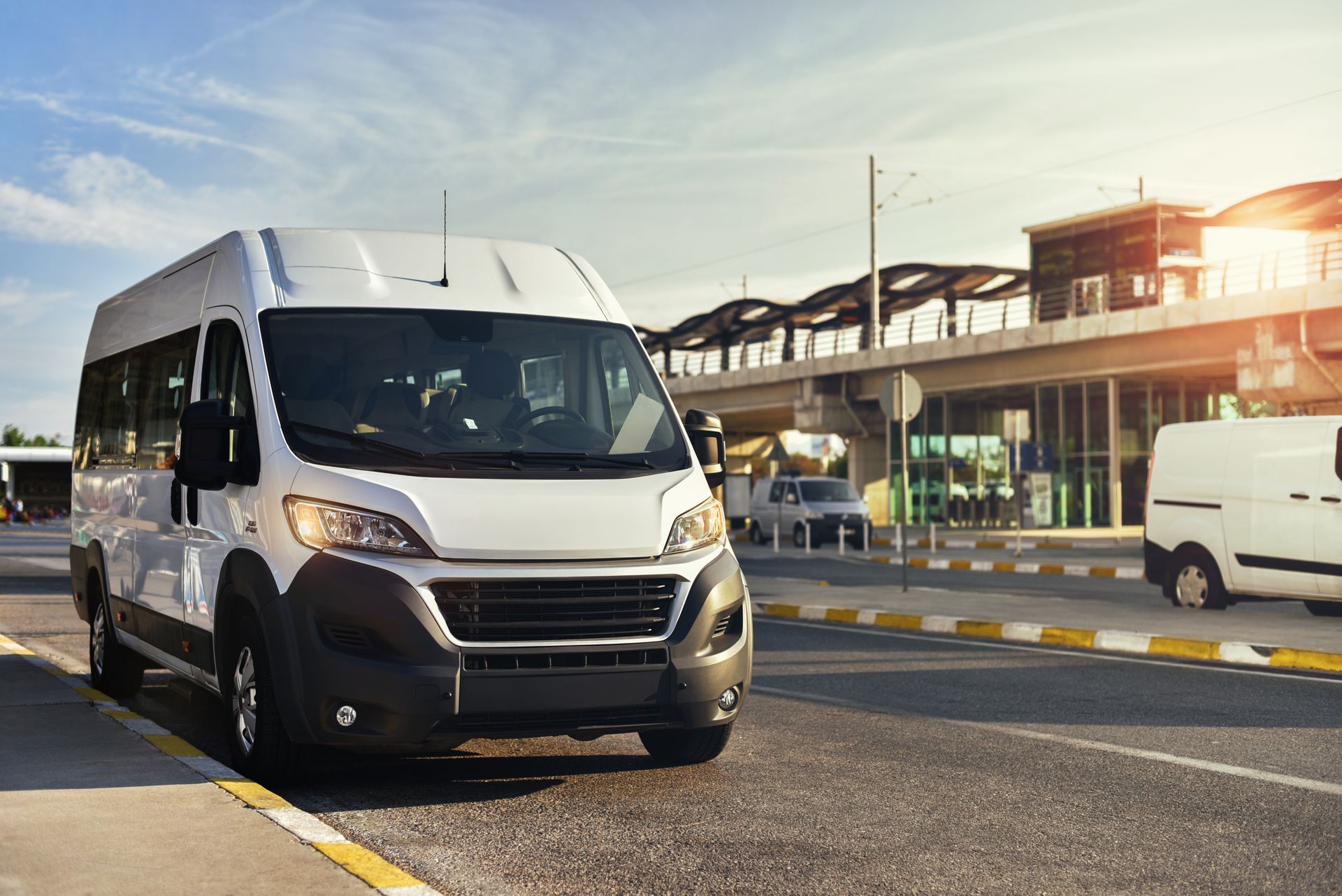 White shuttle van driving on a sunny roadway near an airport terminal