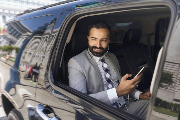 Businessman smiles from the inside of a limousine as he uses a smartphone and earbuds connected to i