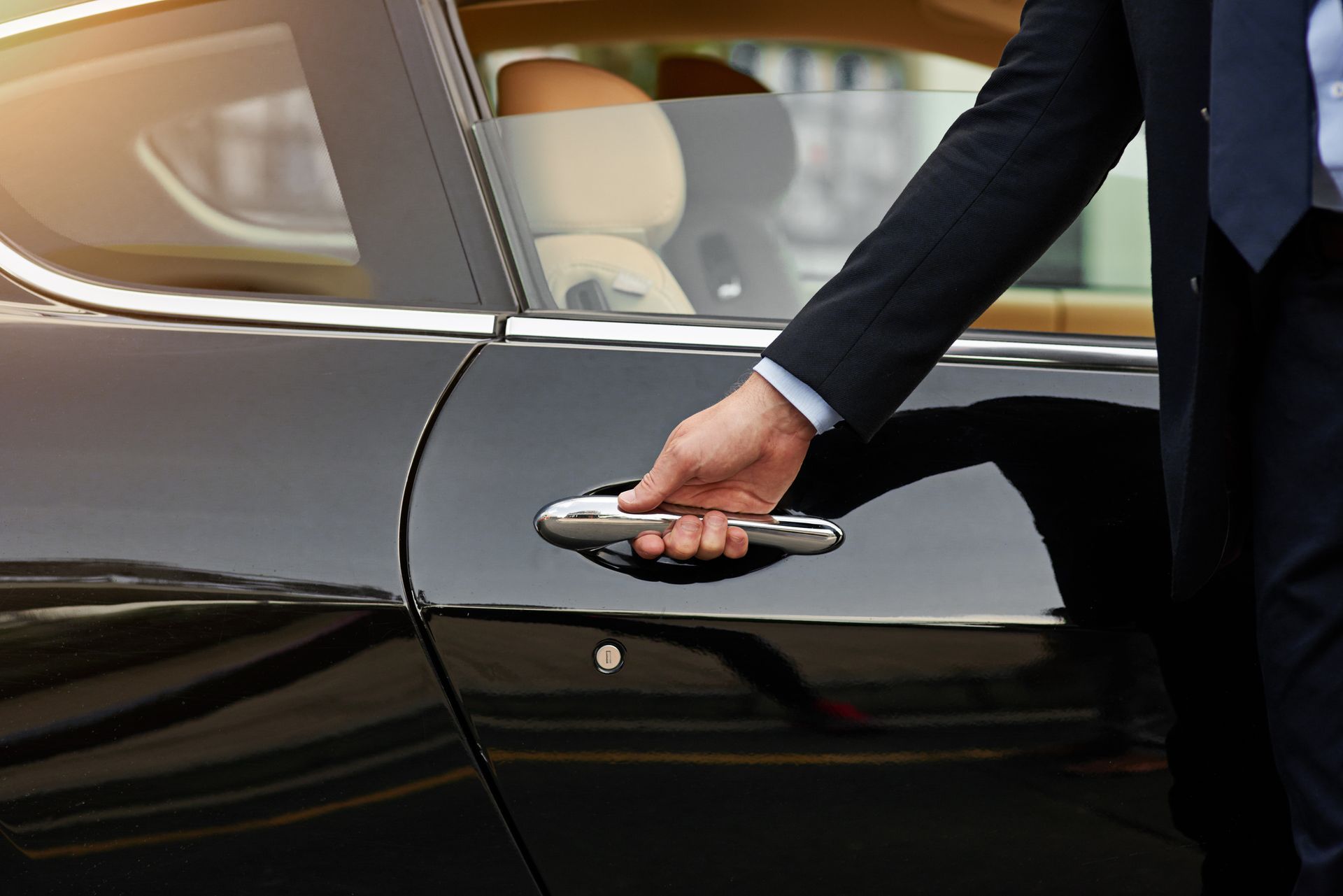A man in a suit and tie is opening the door of a black car. A man in a suit and tie is opening the door of a black car.