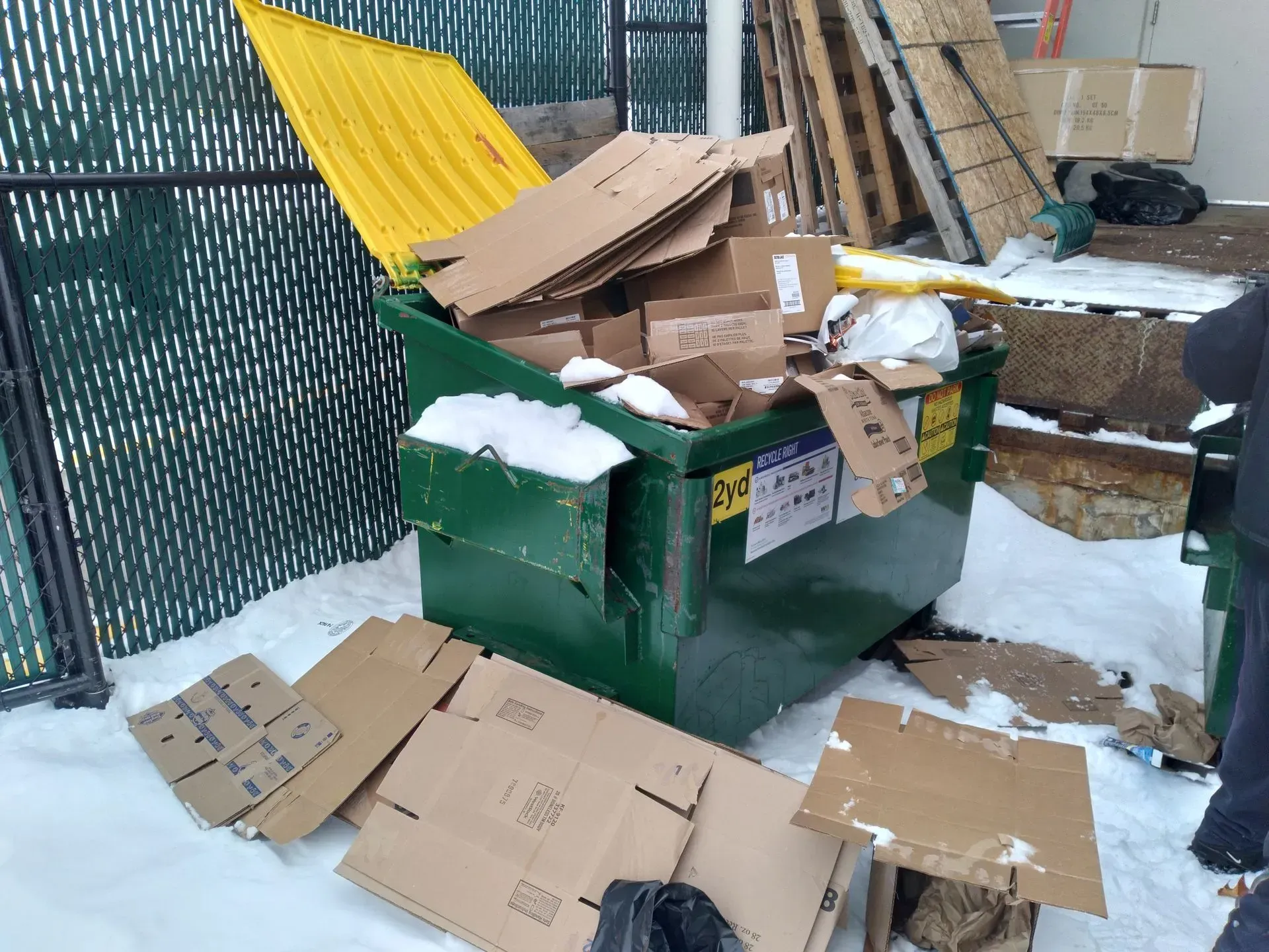 A green dumpster filled with cardboard boxes in the snow