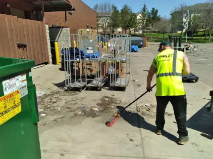A man in a yellow vest is sweeping the sidewalk