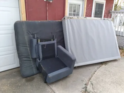 A mattress and a chair are sitting on the sidewalk in front of a garage door.