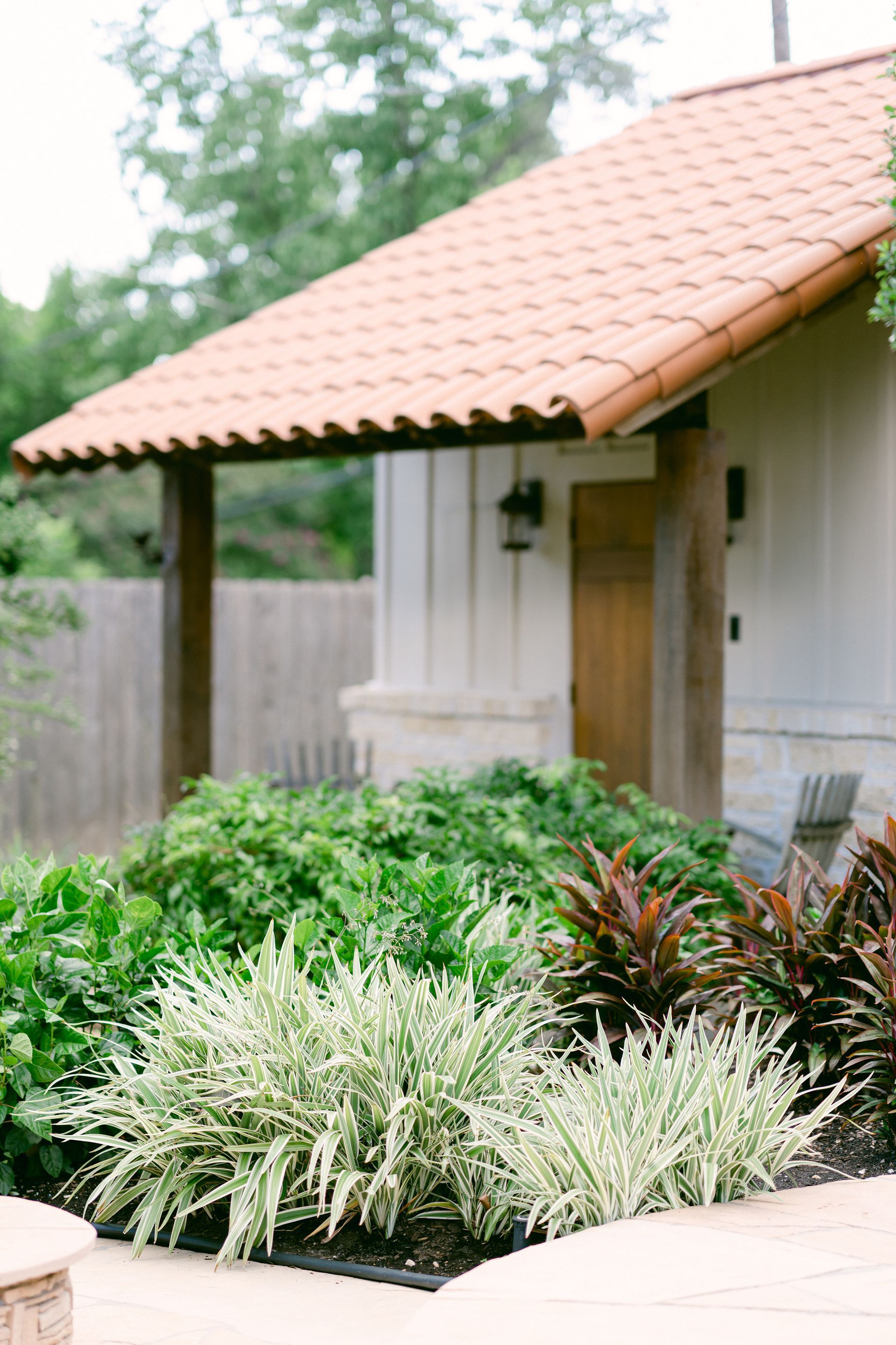 A pool house with a tiled roof and a lush green garden in front of it.