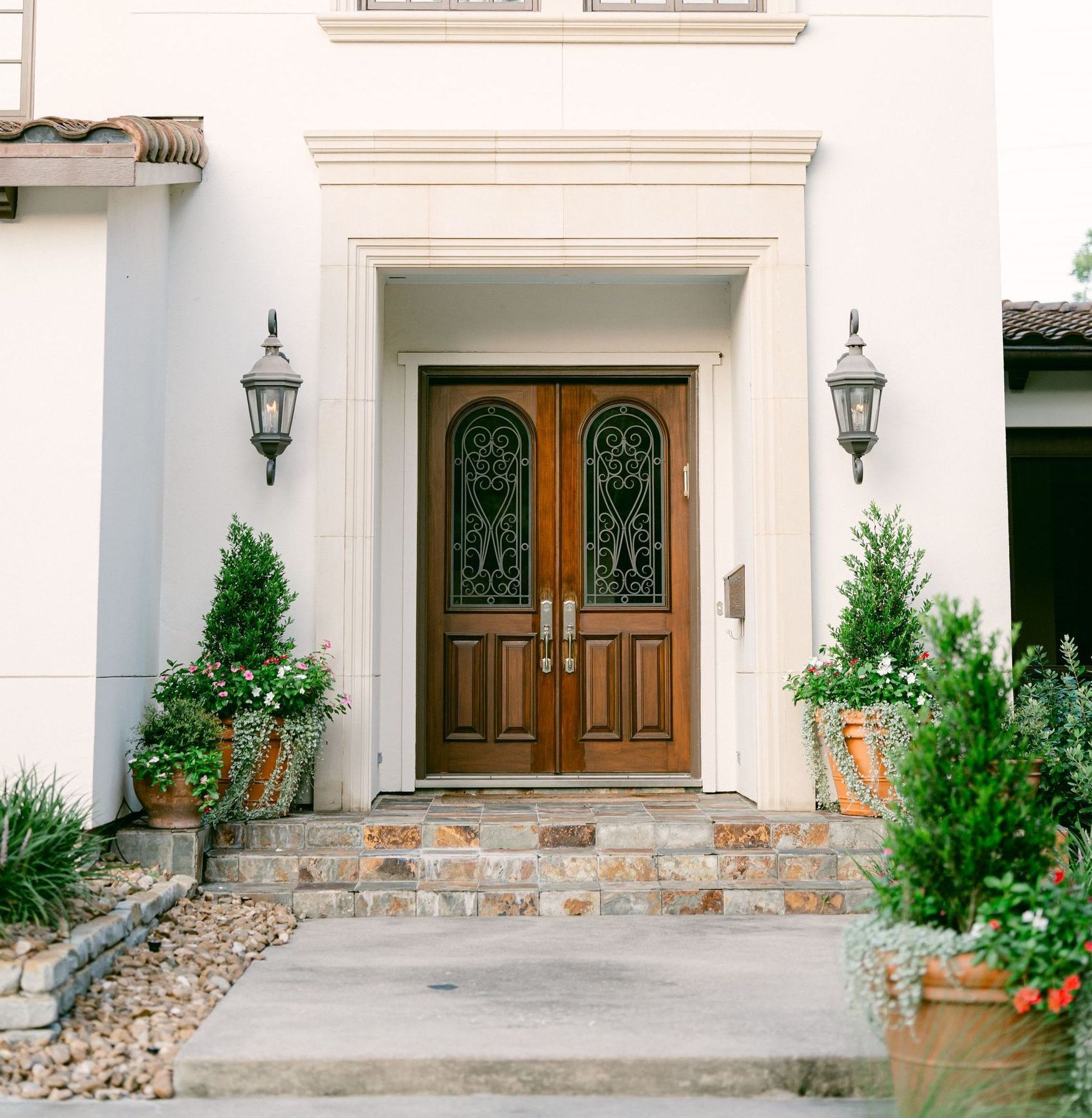 A white house with a wooden door and stairs and potted plants.