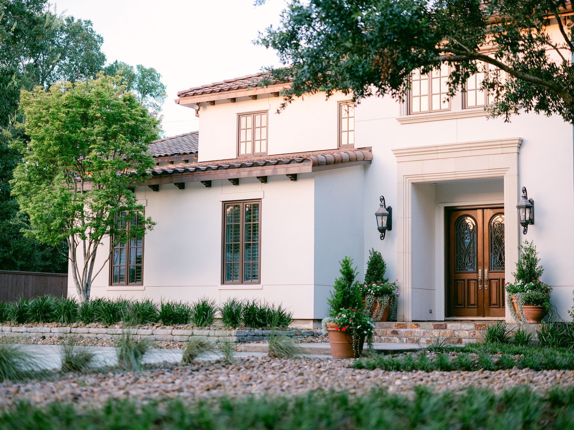 A white house with a tiled roof is surrounded by trees and bushes