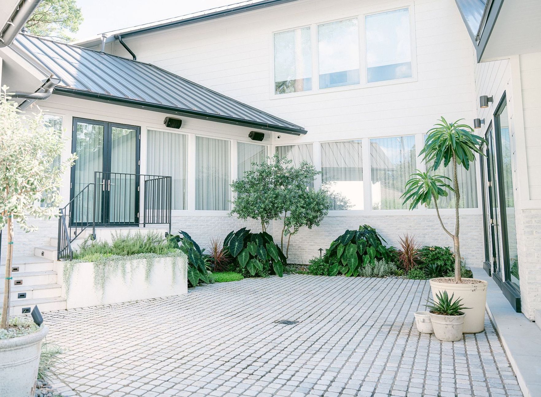 A white house with a black roof and a brick patio in front of it.