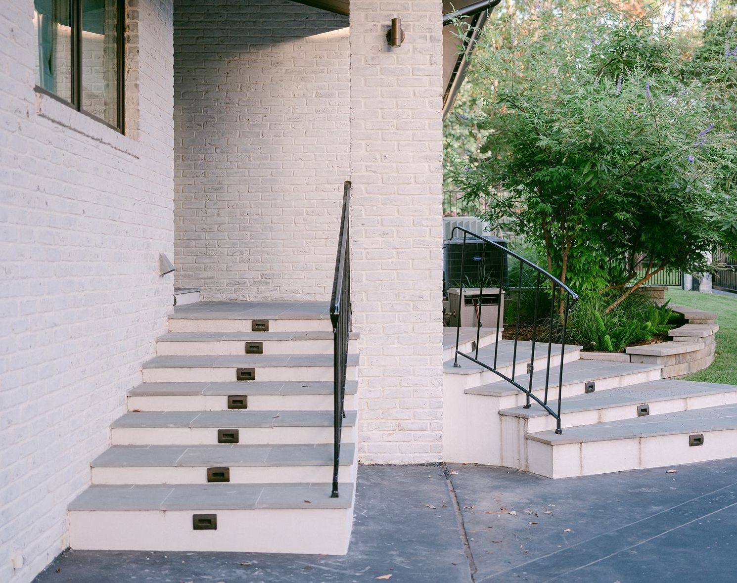 A white brick house with stairs and a black railing
