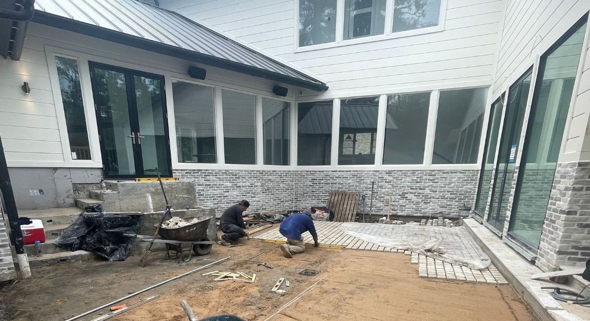 A couple of men are working on a patio in front of a house.