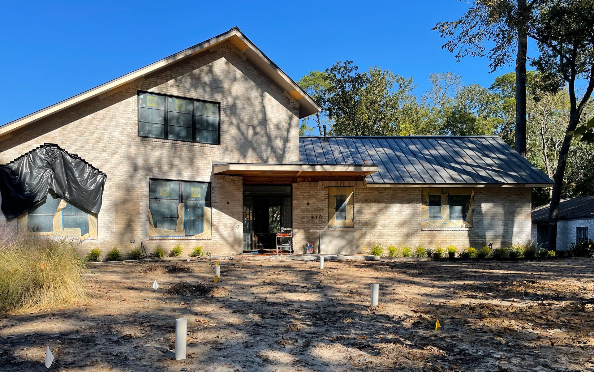 A large brick house with a metal roof is surrounded by trees and dirt .