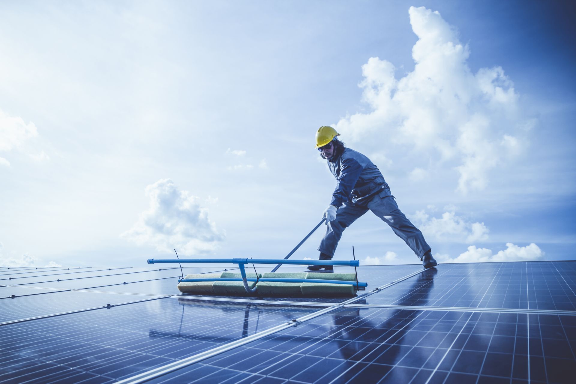 Worker cleaning solar panels on a rooftop under a bright blue sky
