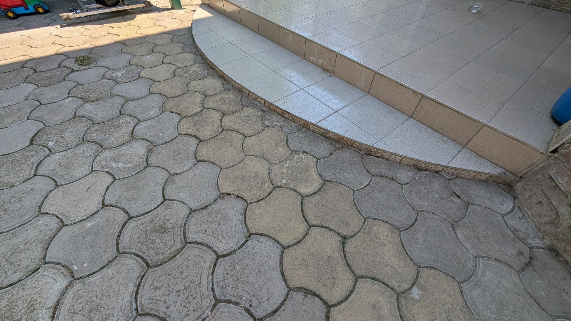 Curved tiled sidewalk beside a concrete step and hexagonal paver walkway.