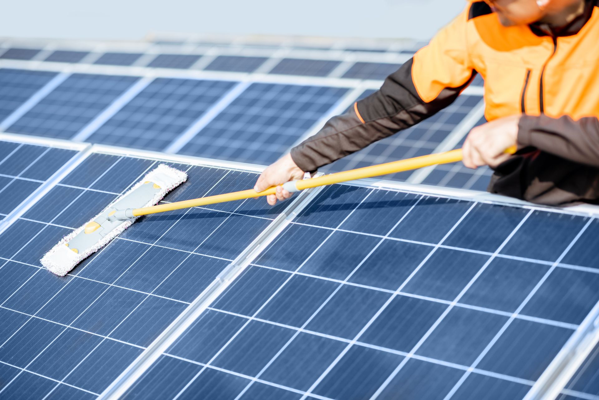 Worker cleaning blue solar panels with a squeegee on a rooftop