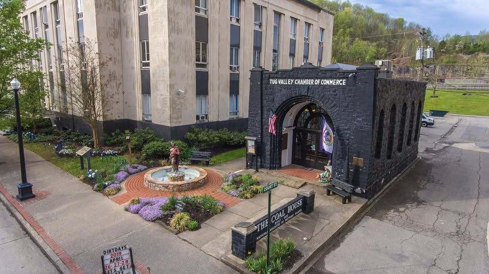 Stone building entrance with archway, landscaped flower bed, and sidewalk on a cloudy day