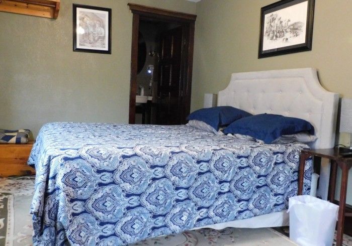 Bedroom with blue patterned bedspread, white headboard, and framed art on green walls