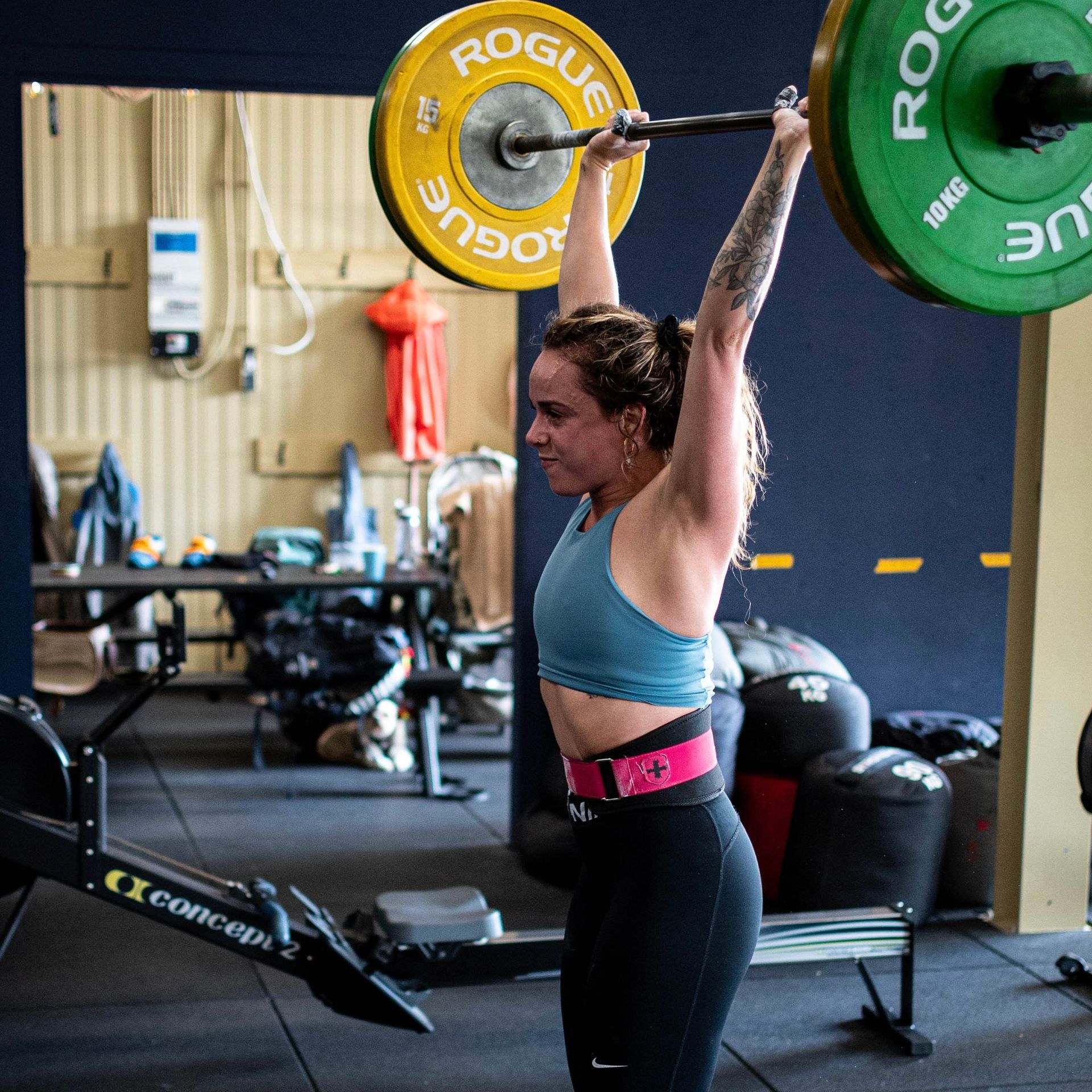 Een vrouw neemt een gewichthefhouding aan en tilt een halter boven haar hoofd in een sportschool. Ze draagt ​​een gewichthefgordel.