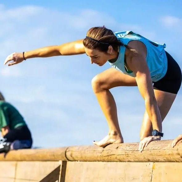 Vrouw in sportkleding, die zich vastklampt aan een houten balk, aan het klimmen in de buitenlucht.