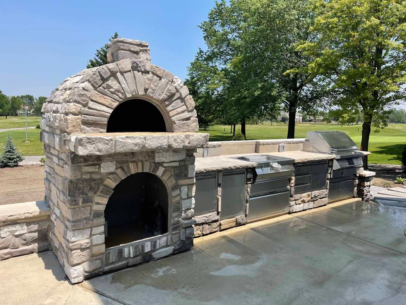 A large stone oven is sitting next to a stainless steel grill.