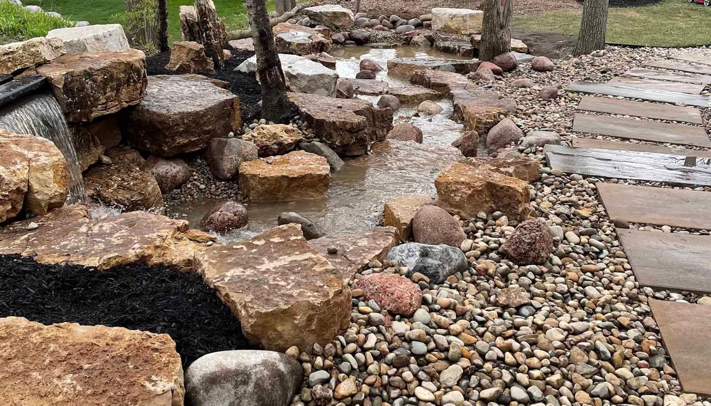 A stream running through a rocky area next to a wooden walkway.