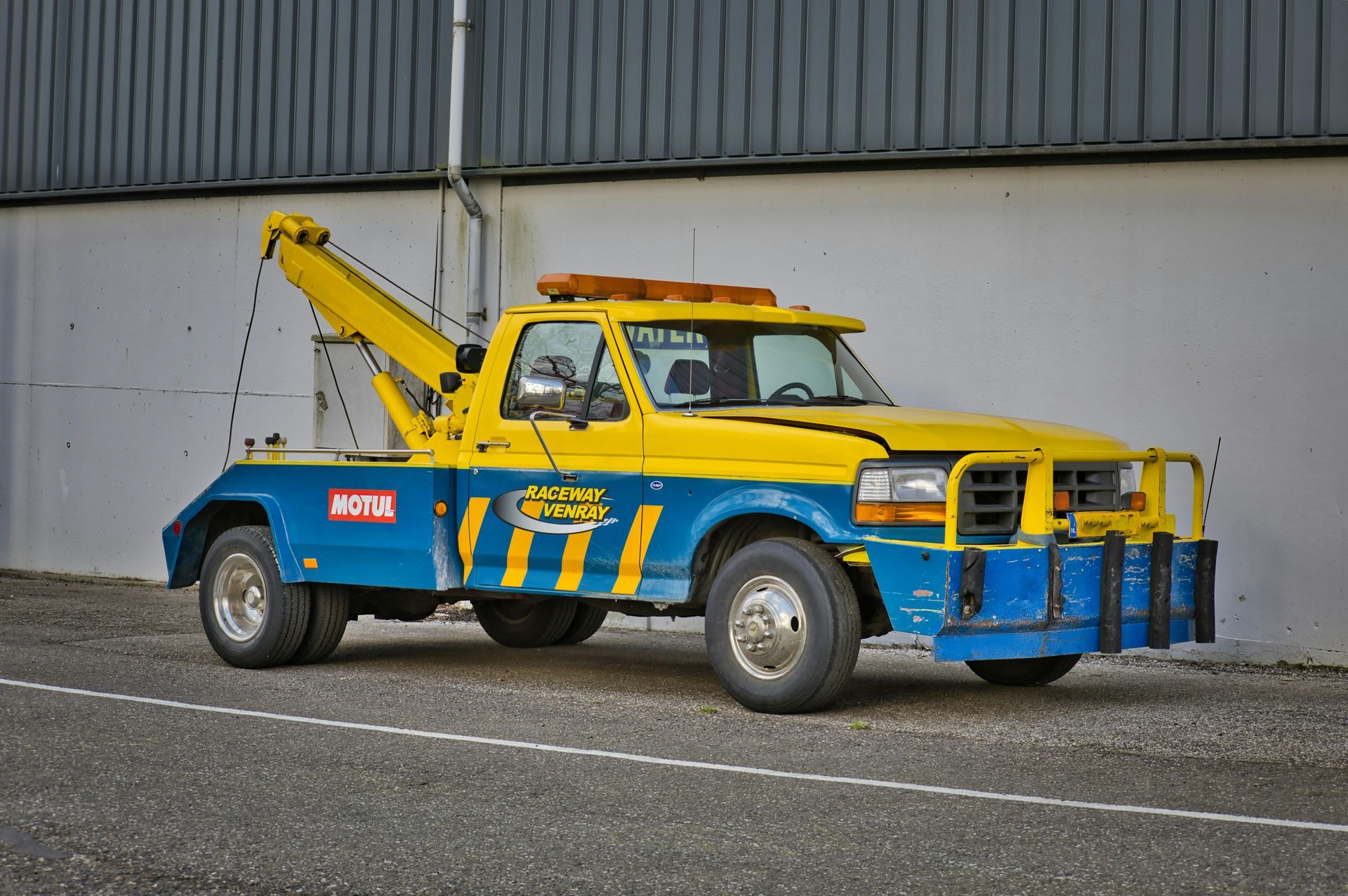 Yellow and blue tow truck parked indoors against a white wall