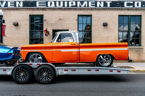 Orange classic pickup truck on a car hauler trailer outside a brick building