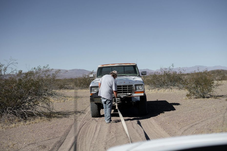 Tow truck pulling a vehicle stuck in desert sand with a person guiding the tow line