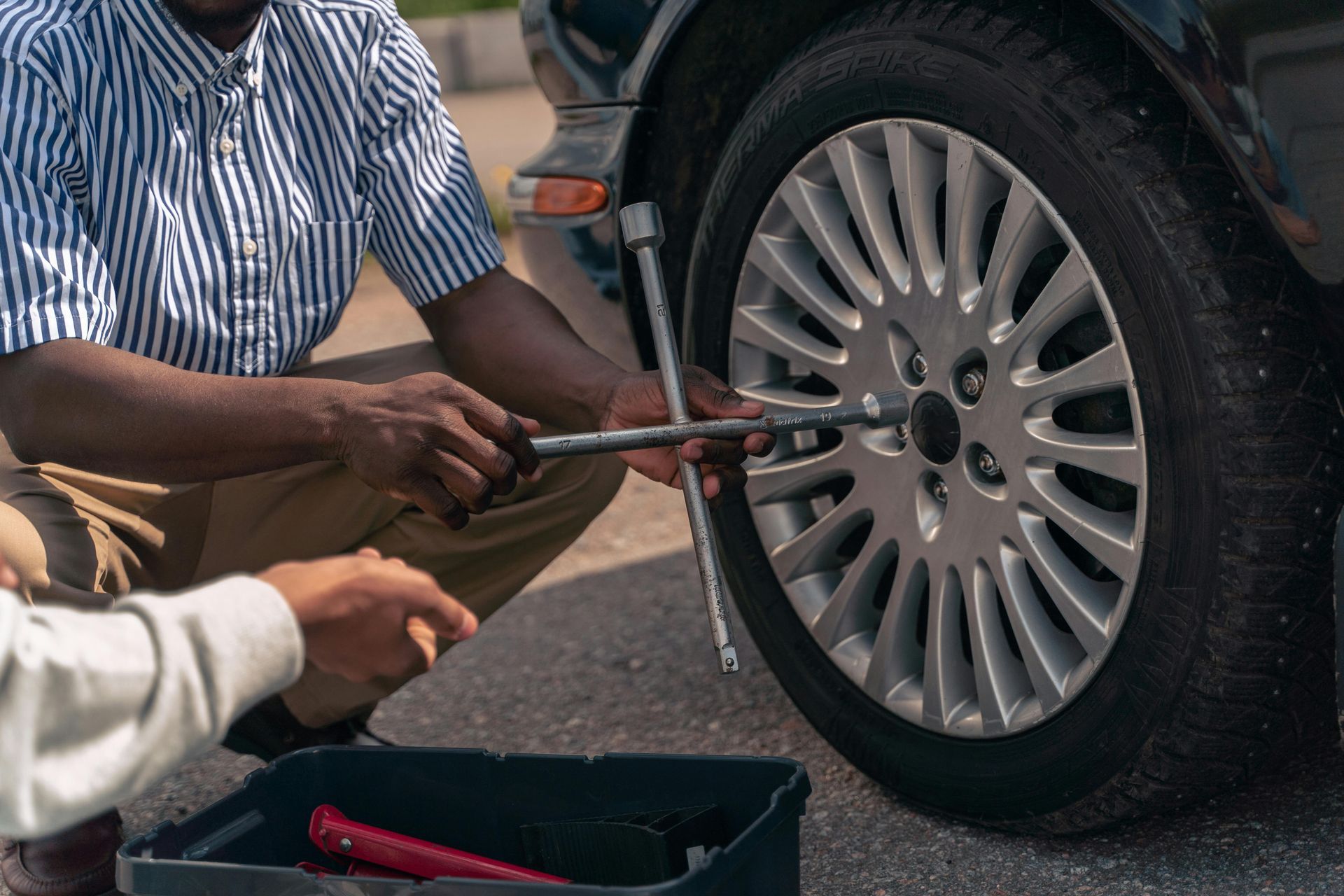 Two people use a wrench to tighten a car wheel lug nut on a black vehicle.