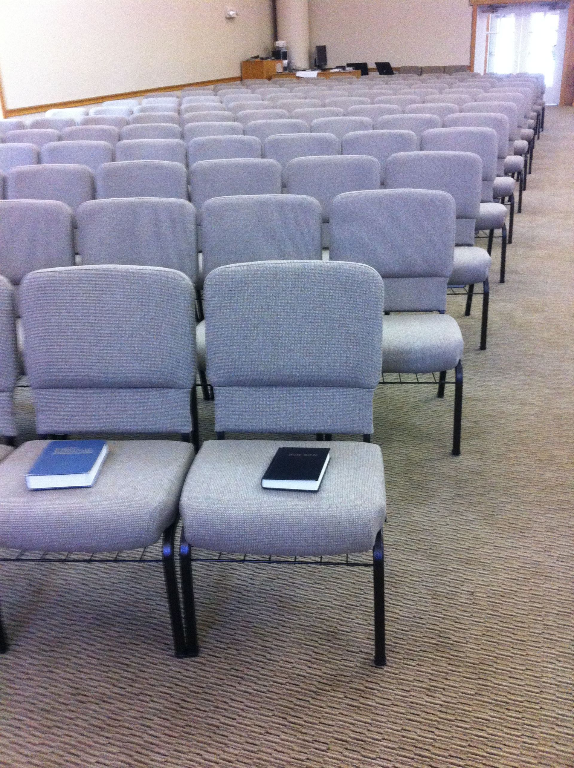 Church sanctuary with rows of gray upholstered chairs and hymnals.