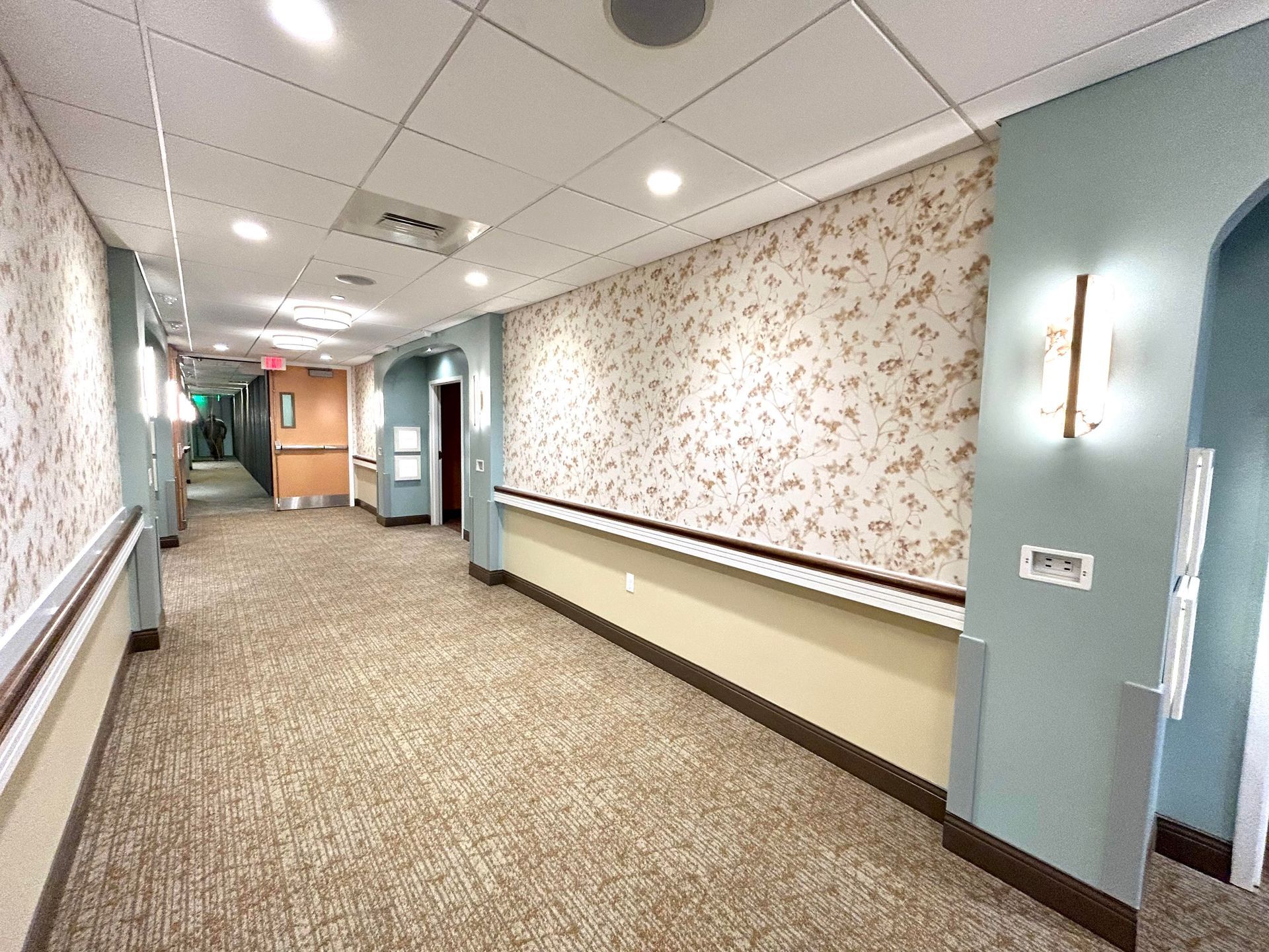 A long hallway in a hospital with a floral wallpaper on the wall.