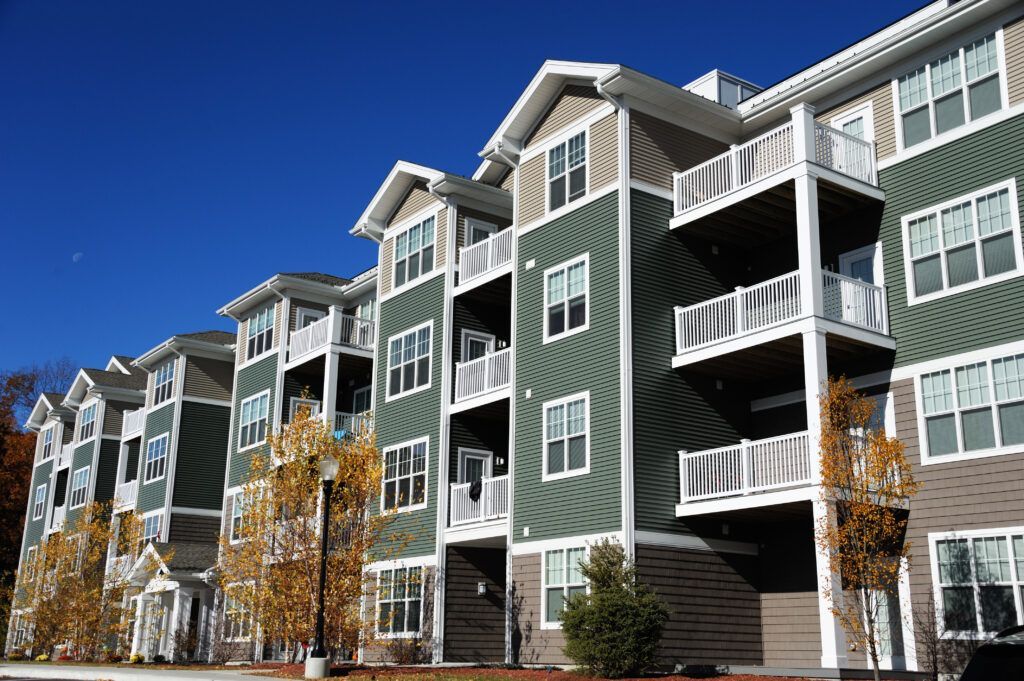 Green multi-story apartment complex with white balconies against blue sky.