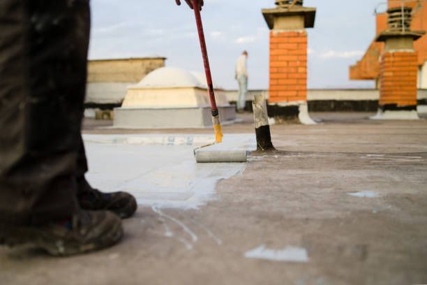Professional roofer rolling elastomeric coating on commercial building rooftop surface.