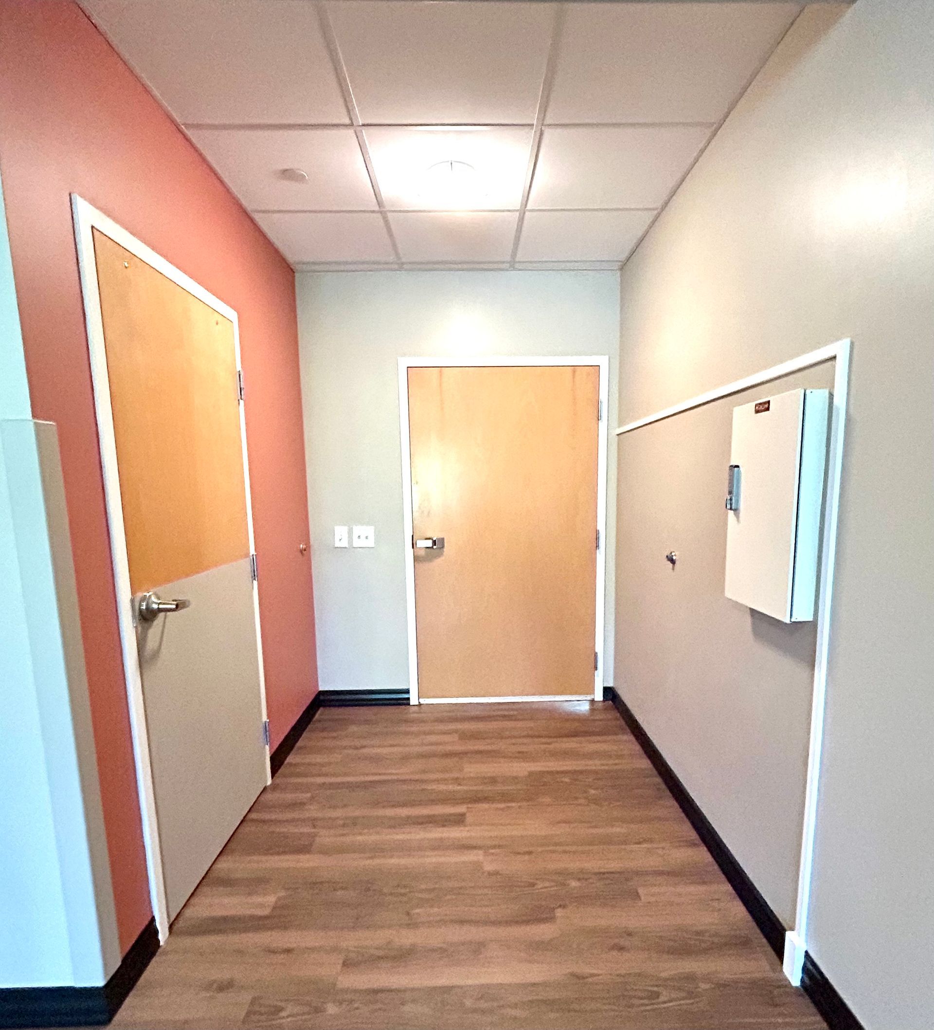 Medical office hallway with wooden flooring and coral accent wall.