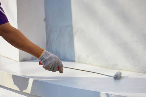 Professional applying white silicon roof coating with roller on commercial flat roof surface