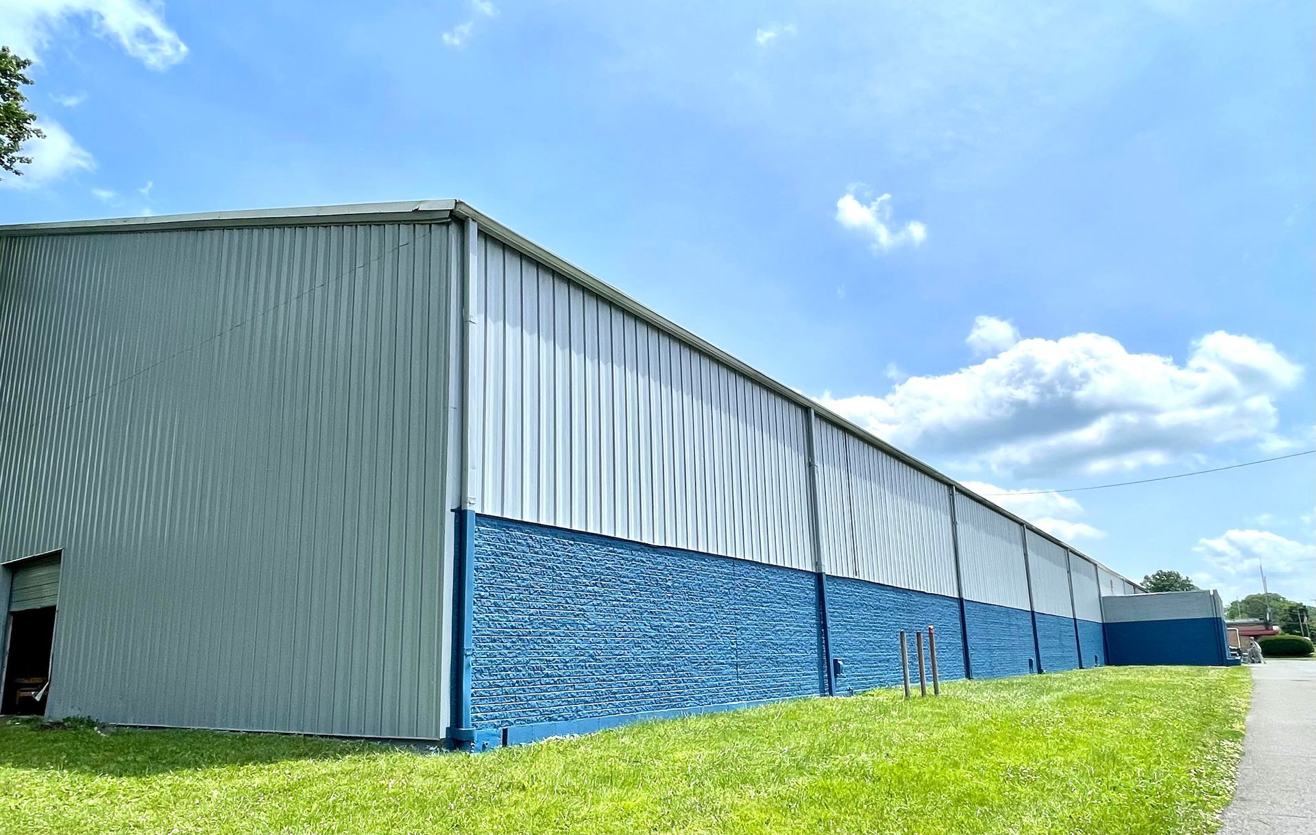 A large building with blue and white walls is sitting on top of a lush green field.