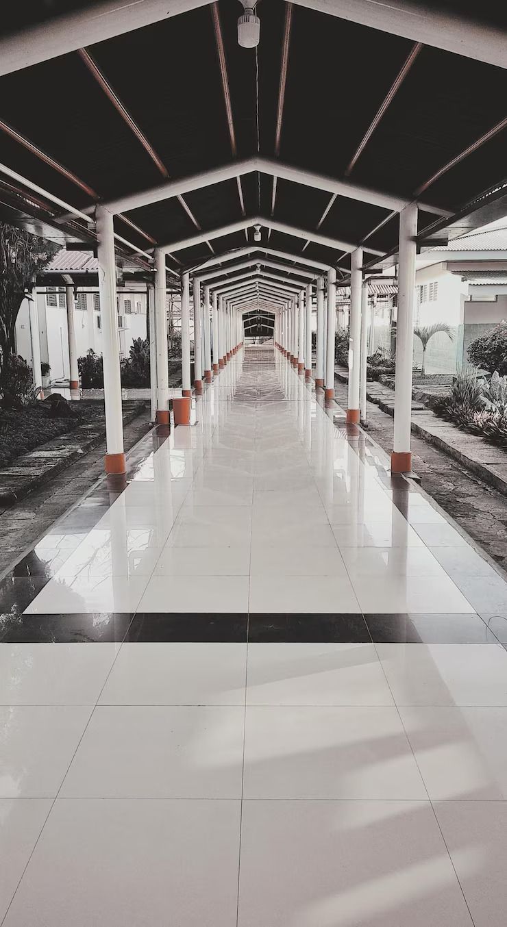 Covered walkway with high-gloss polished tile flooring connecting campus buildings in tropical setting