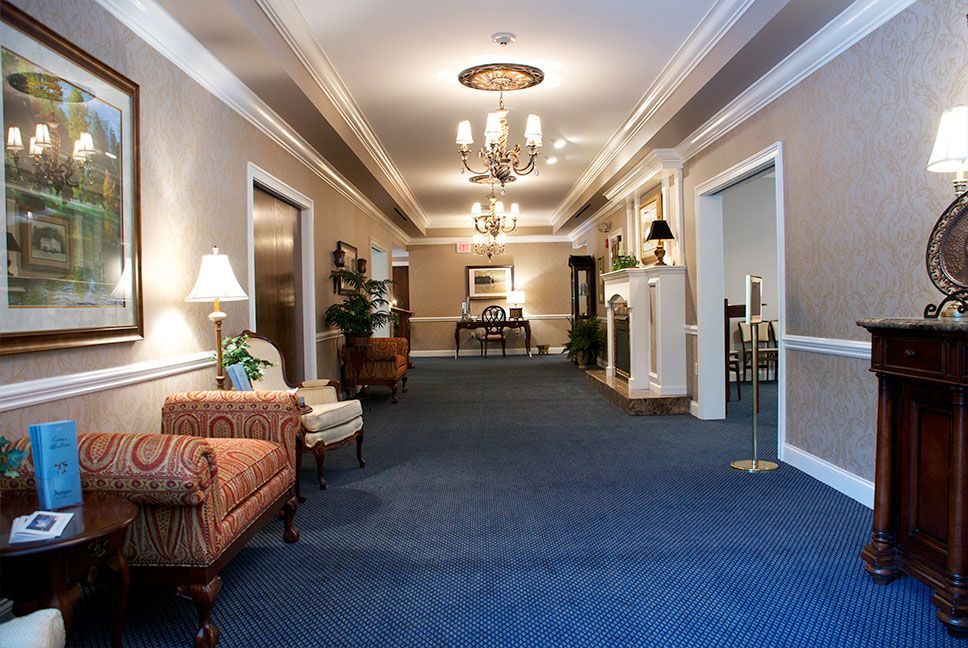Elegant funeral home lobby with traditional furnishings, blue carpeting, framed artwork, and formal lighting