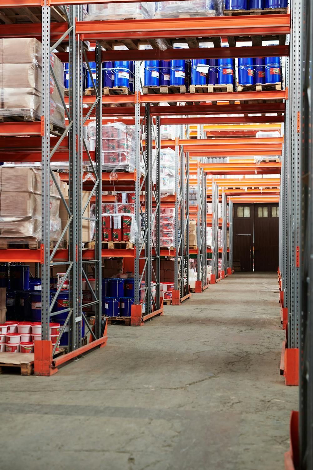 Warehouse storage racks with blue barrels and packaged materials on pallets.