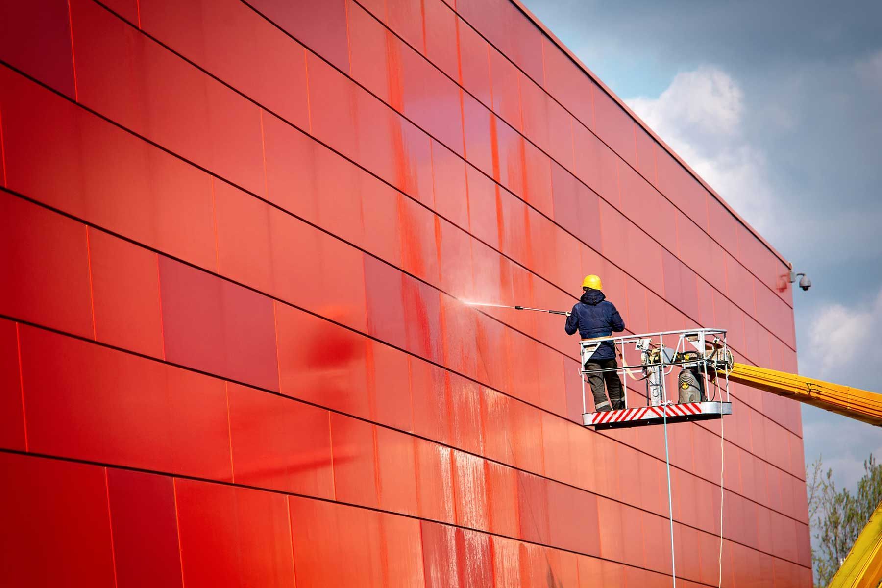 A man is cleaning a red building with a high pressure washer.