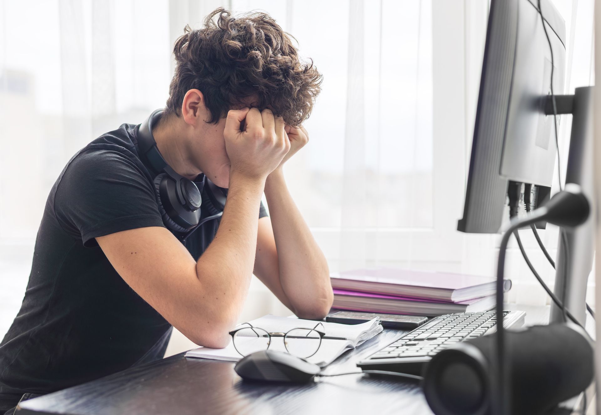 A person sits at a desk with their head in their hands, looking frustrated or exhausted while working on a computer. A person sits at a desk with their head in their hands, looking frustrated or exhausted while working on a computer.