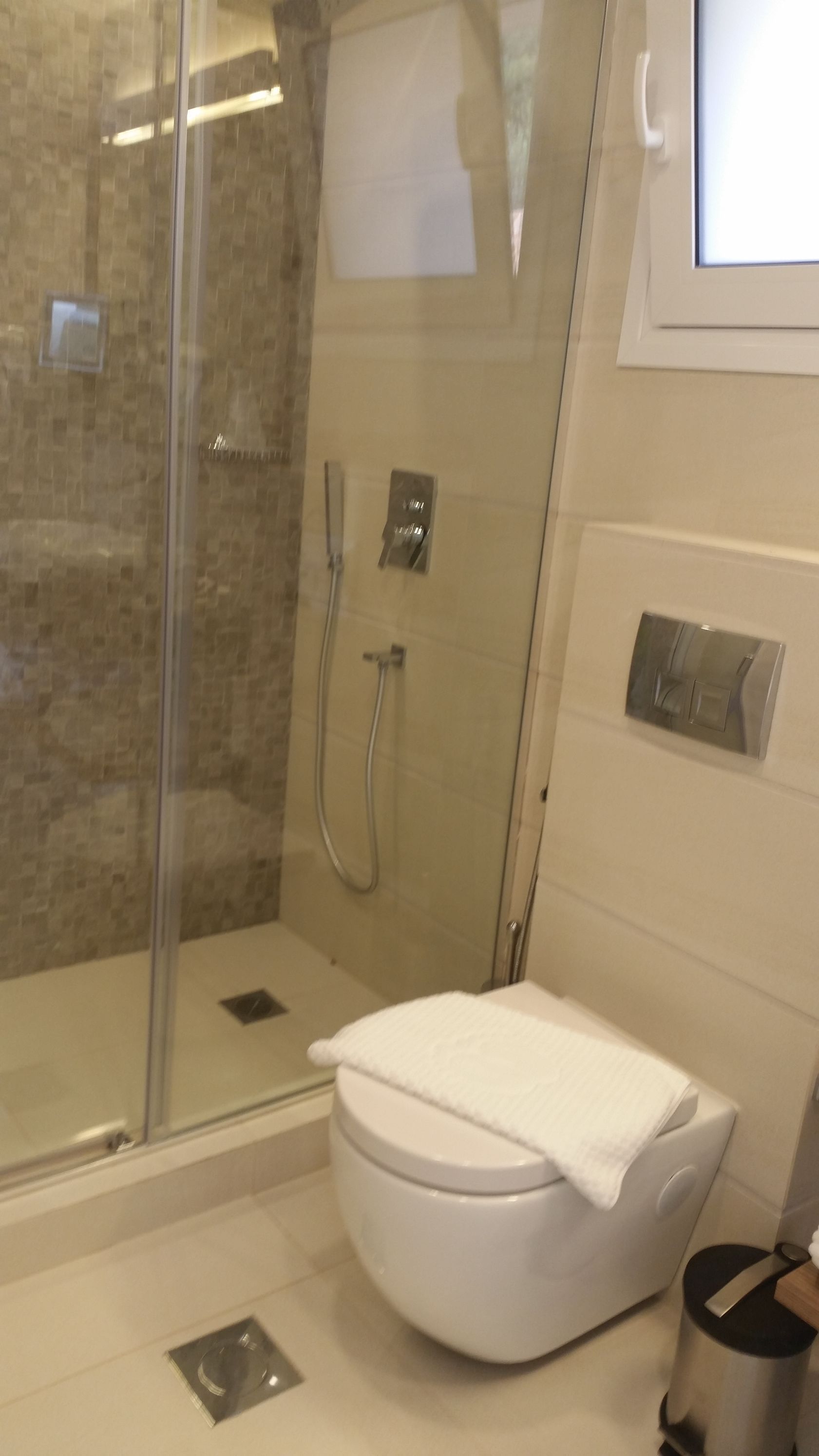 Modern bathroom with walk-in shower, wall-mounted toilet, and window.