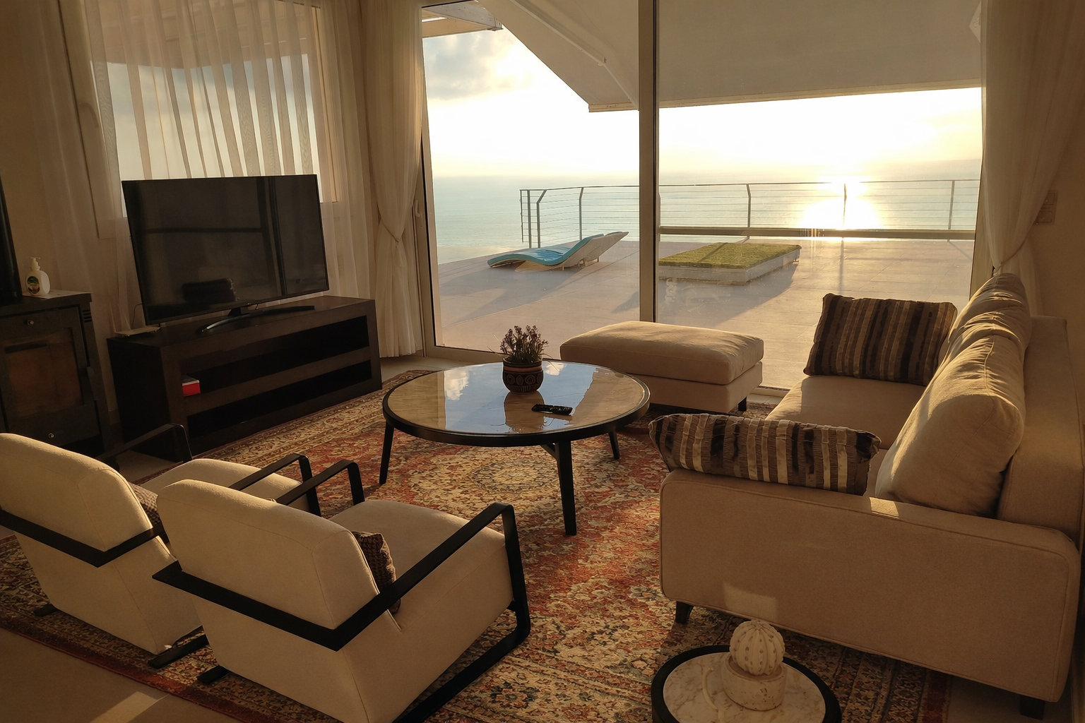 Sunlit living room with ocean view, sofas, chairs, TV, and a coffee table by a large window.