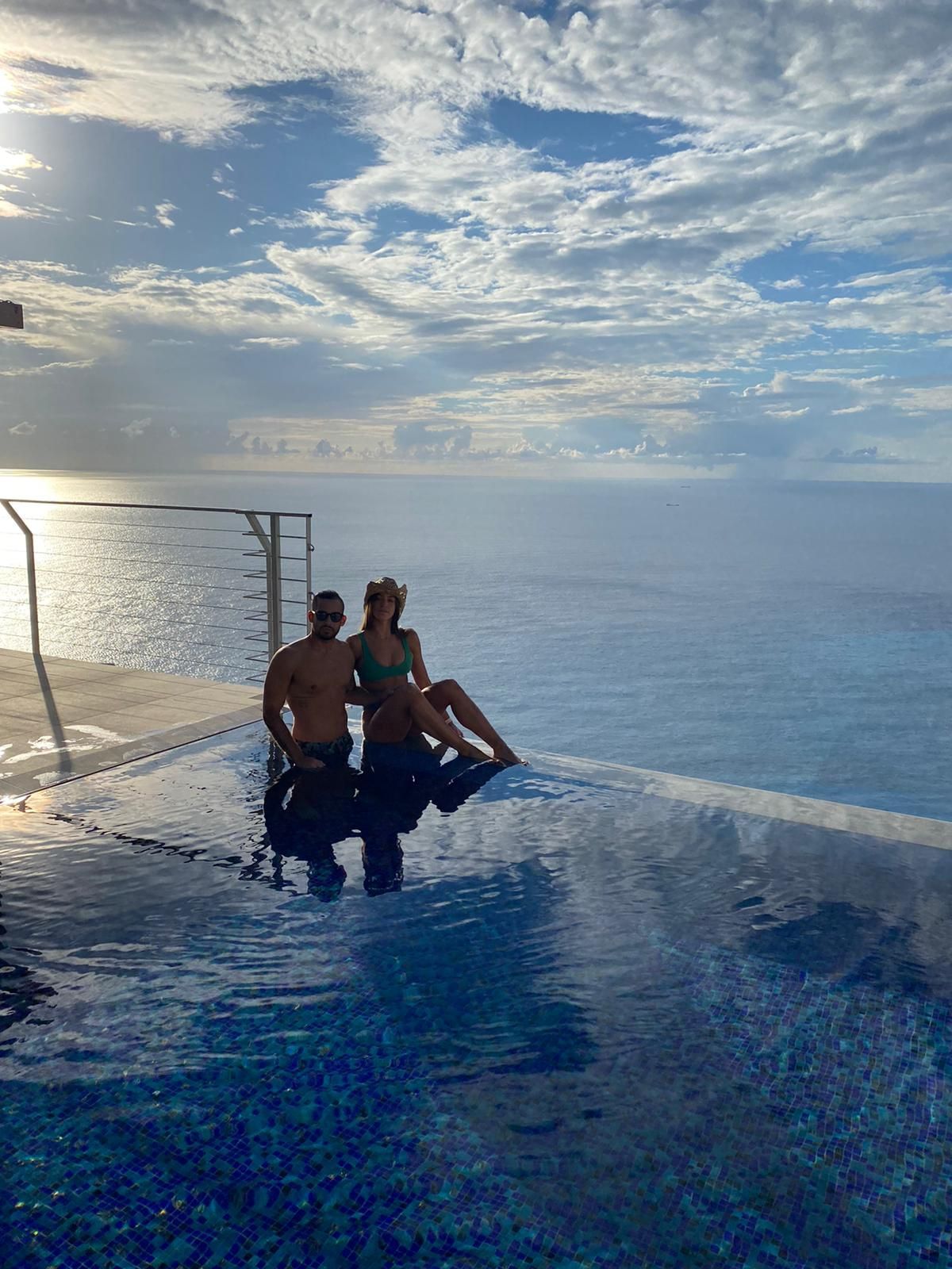 Two people sitting at the edge of an infinity pool overlooking the ocean at sunset