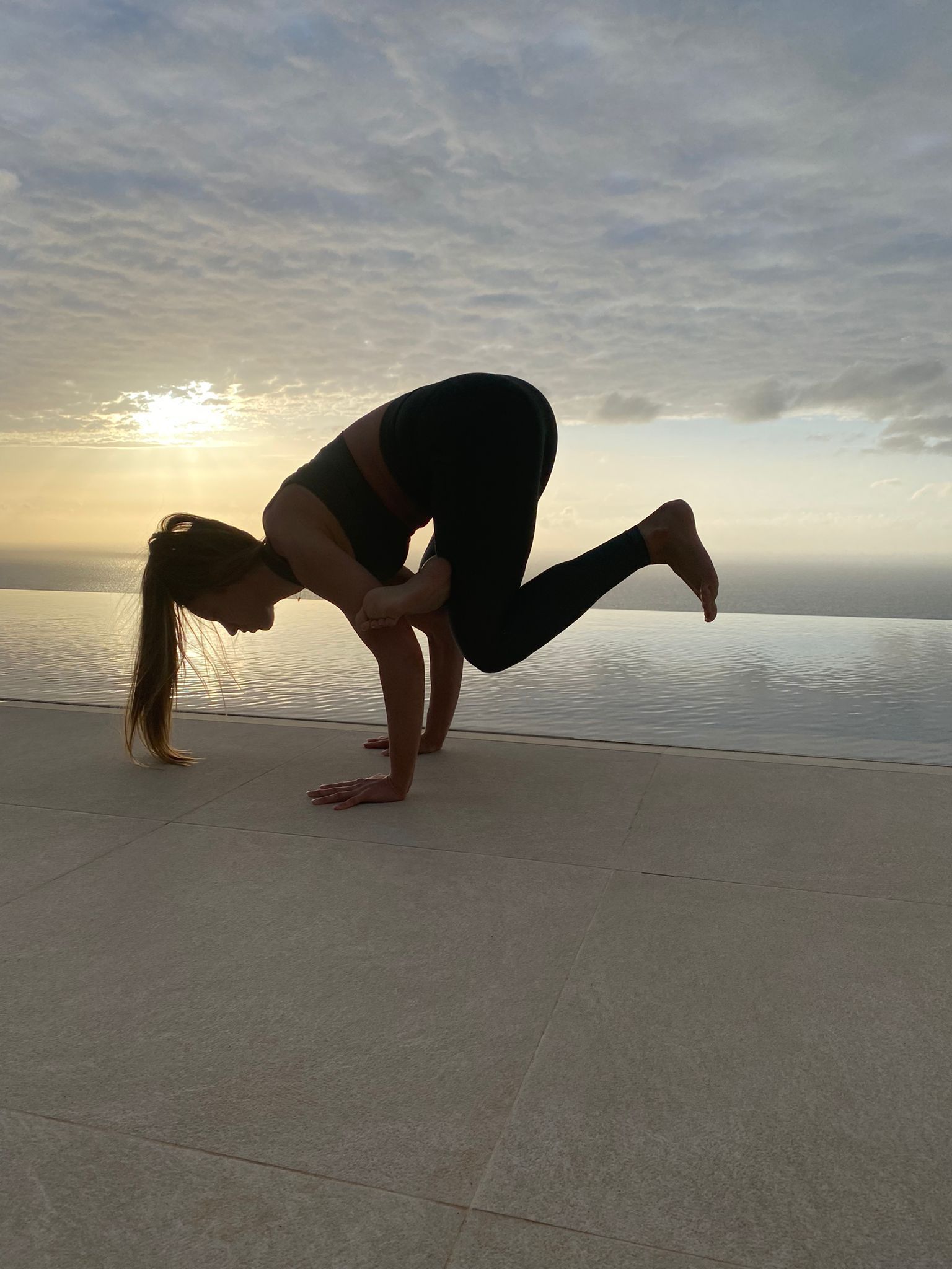 Person balancing in a yoga pose on a sandy beach at sunrise.