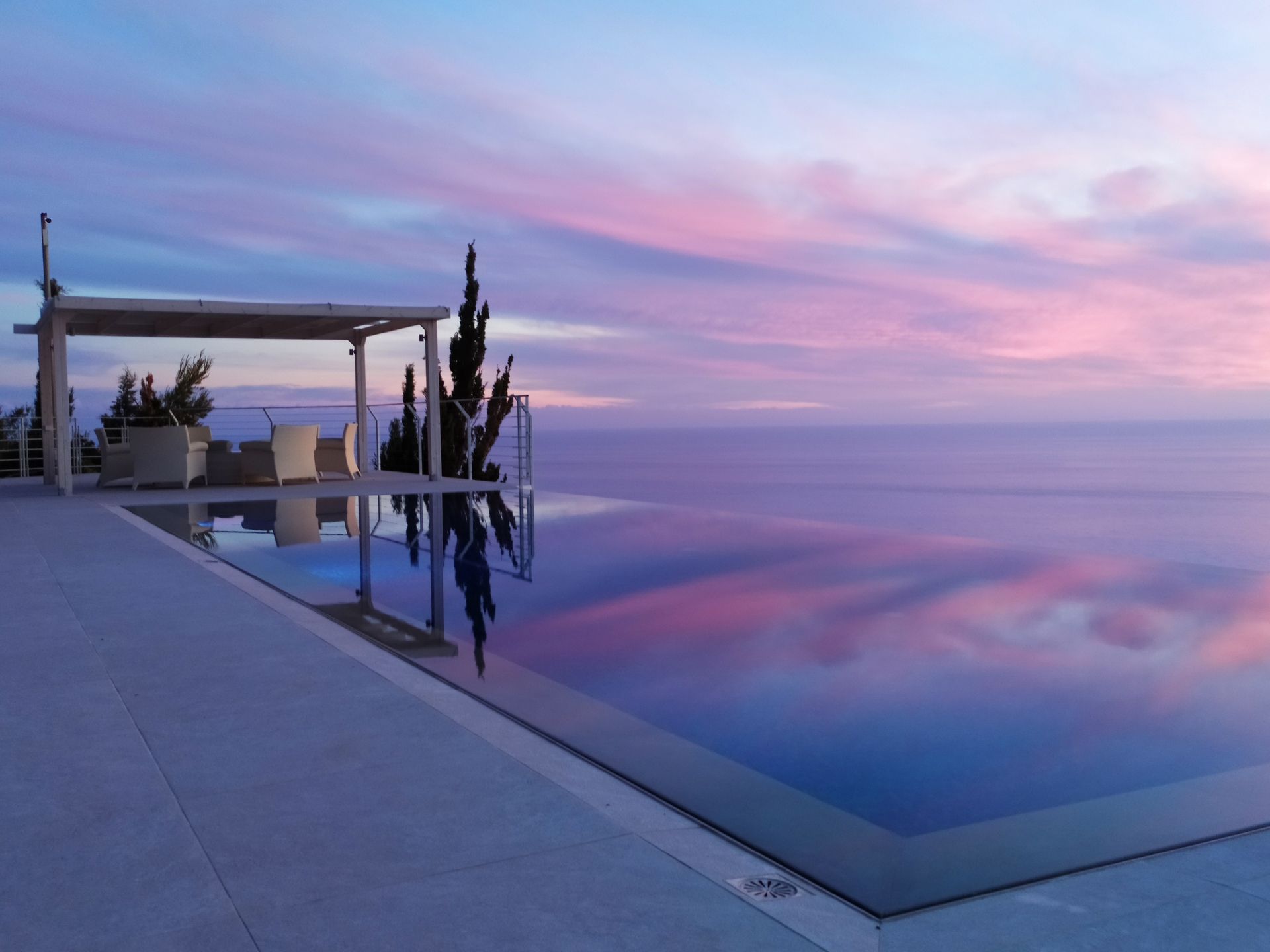 Modern infinity pool at sunset reflecting pink and blue sky beside a minimalist patio