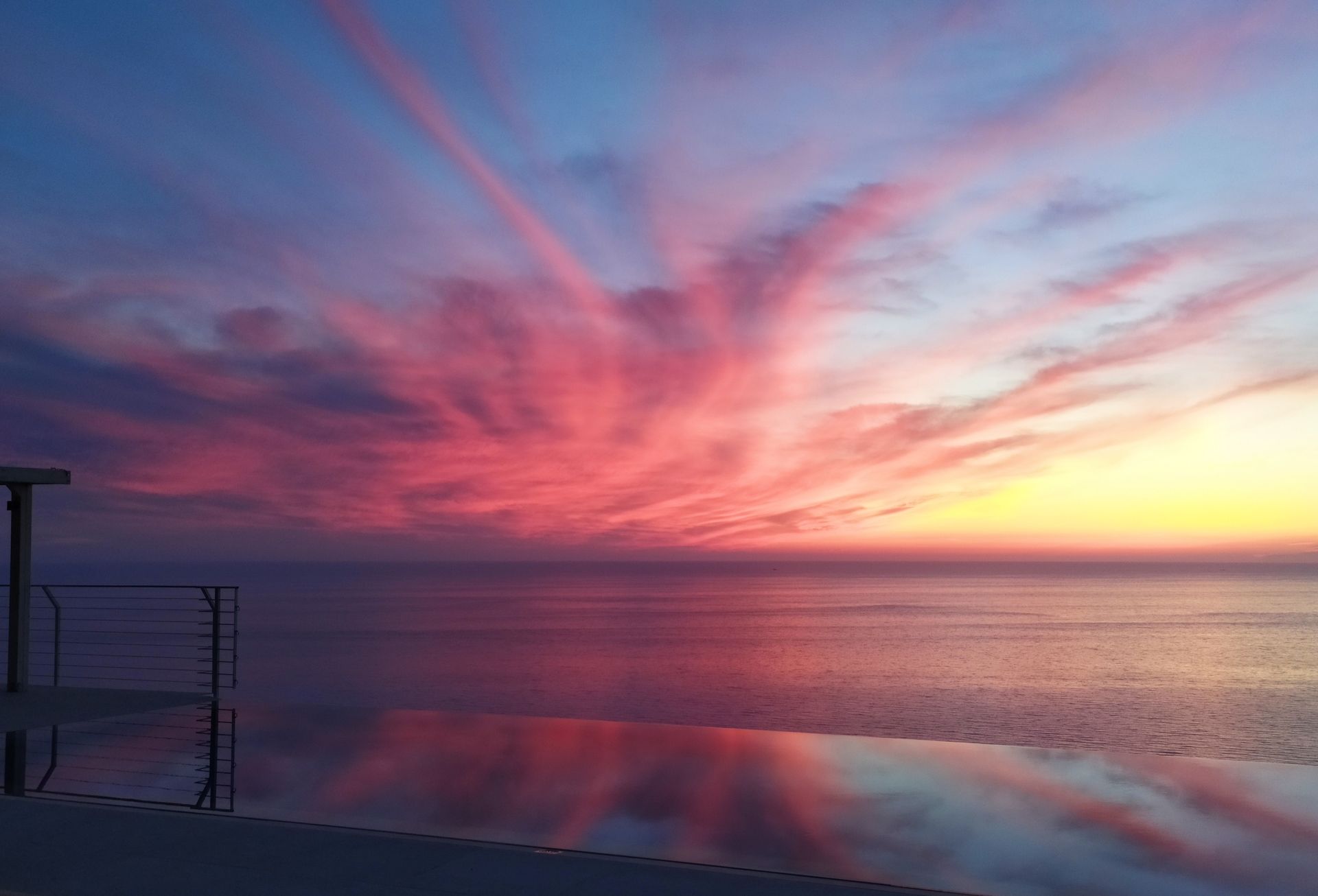 Pink and purple sunset over calm water with reflections and wispy clouds over a dark shoreline