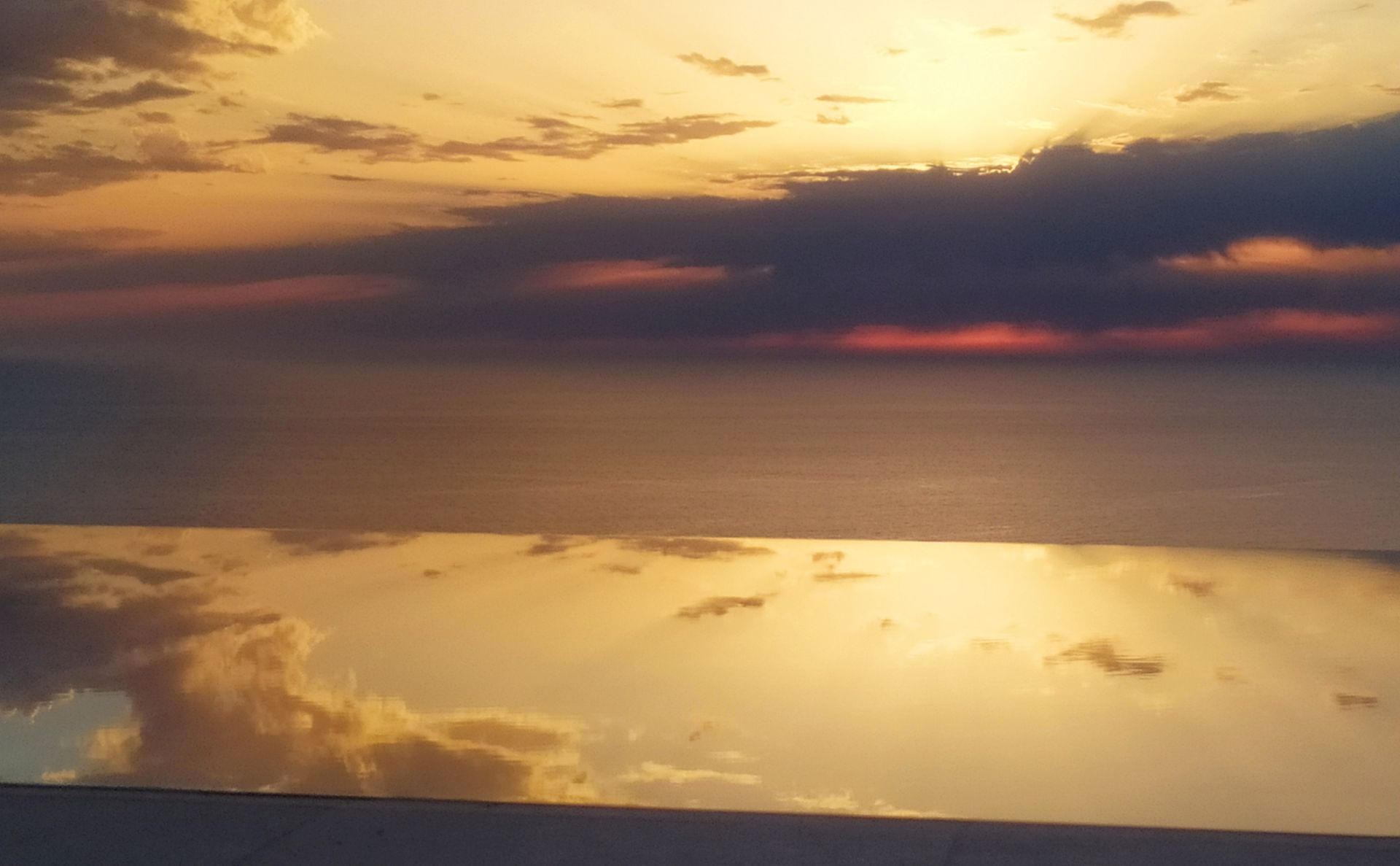 Sunset over calm water, with golden reflections and dark clouds on the horizon.