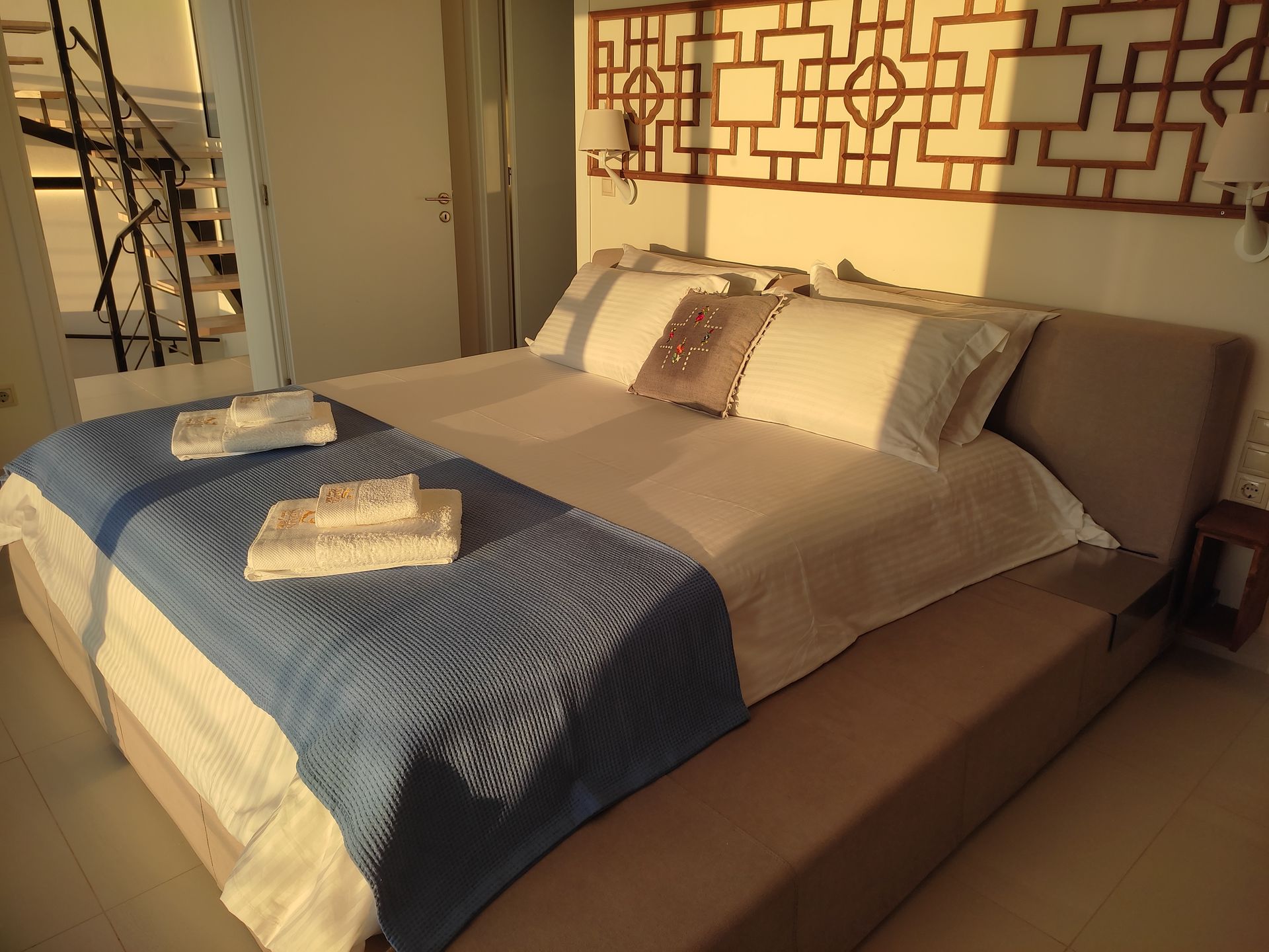 Modern bedroom with a large bed, blue throw blanket, and folded towels near a staircase.