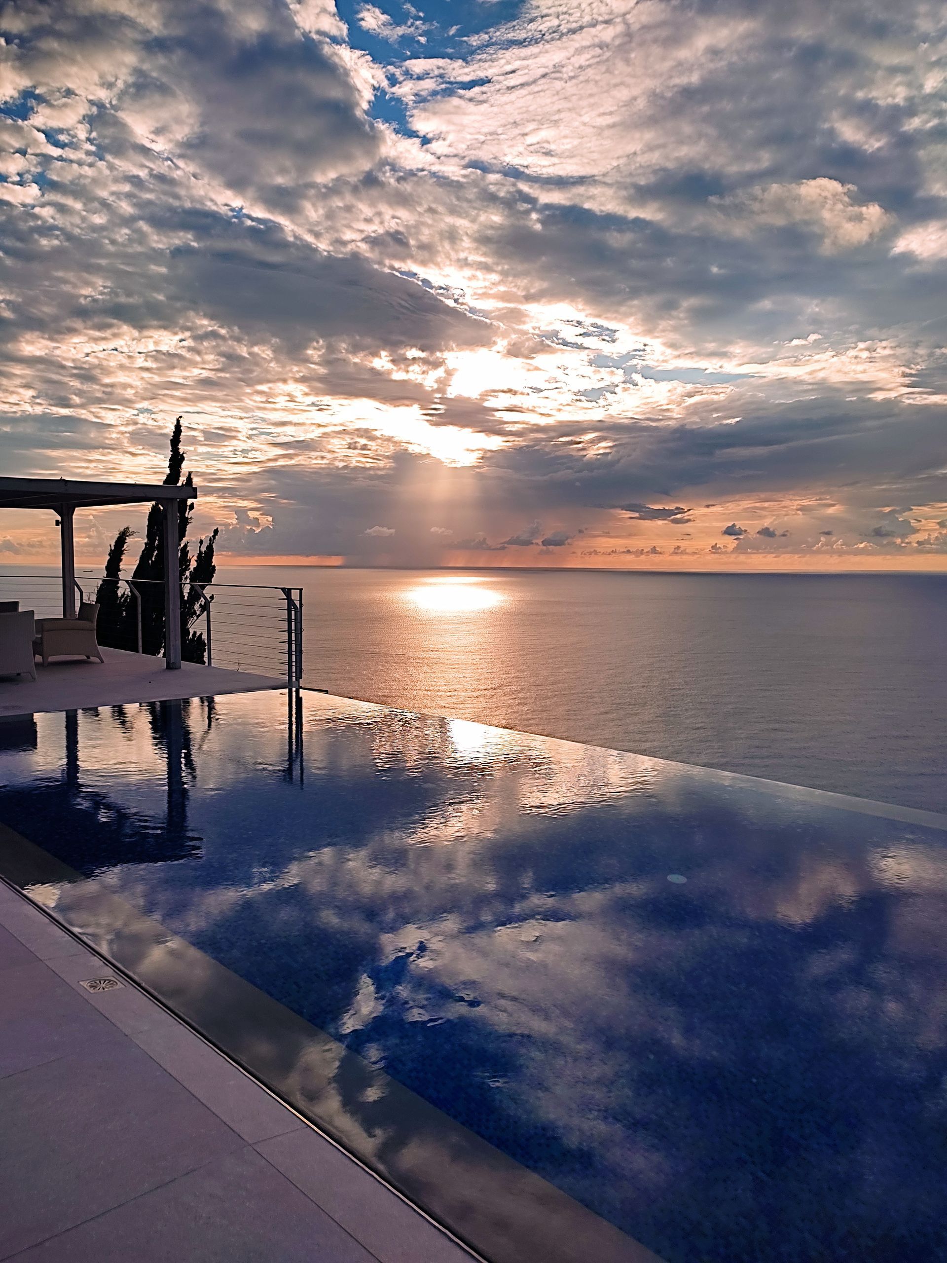Infinity pool at sunset overlooking the ocean, with golden clouds and reflected sky.