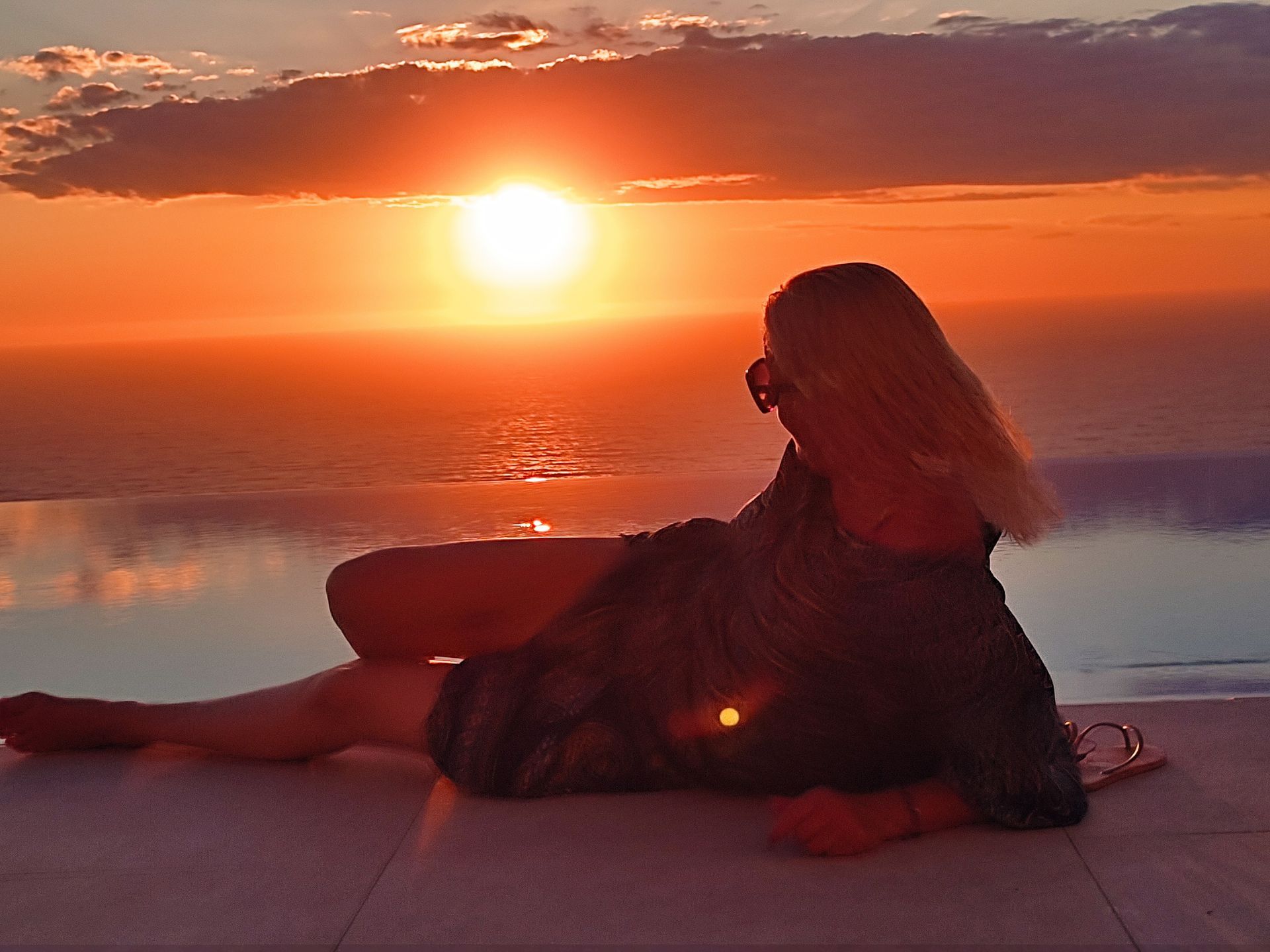 Person reclining on a rooftop at sunset, silhouetted against an orange sky and glowing sun.
