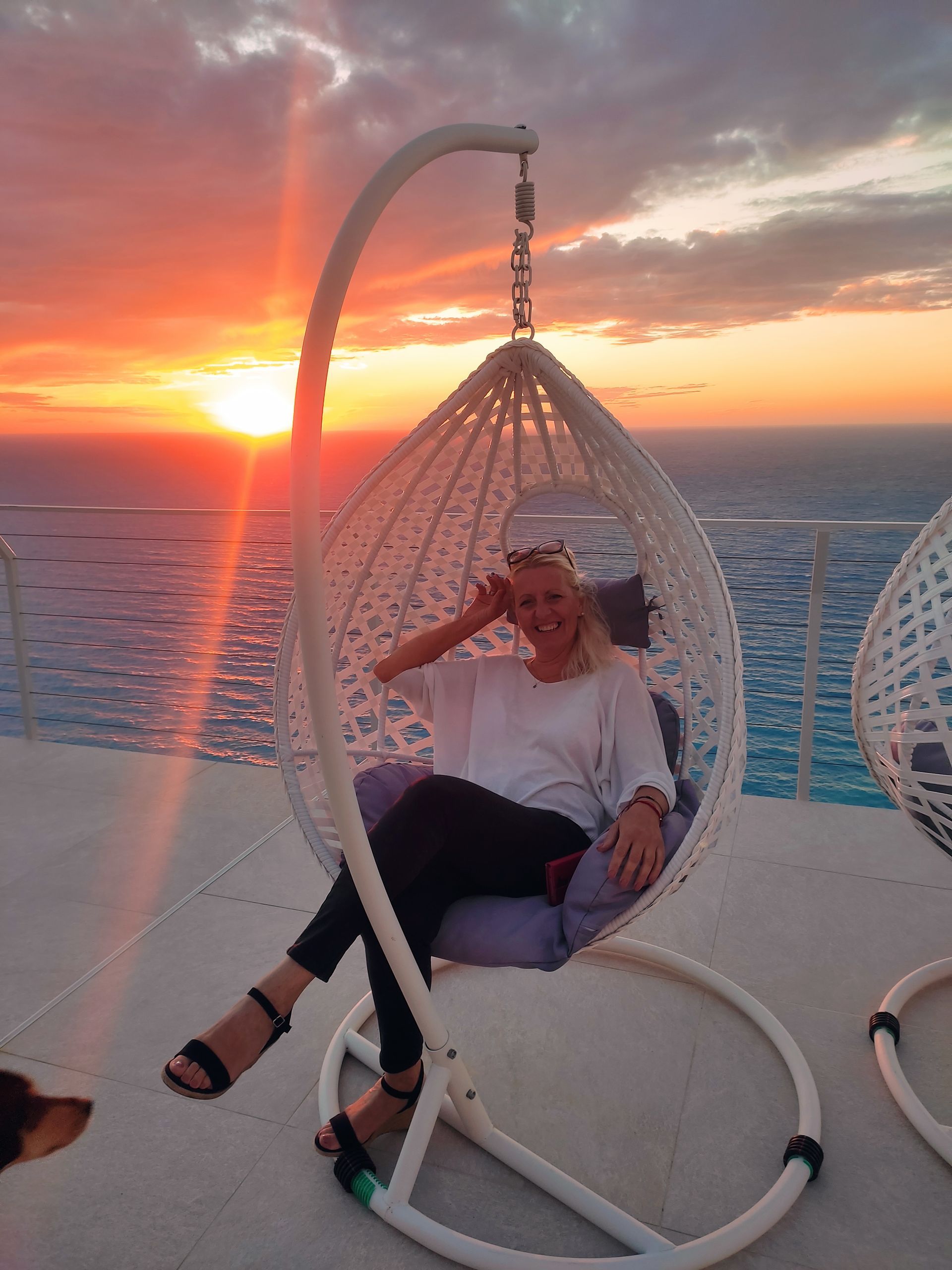Person relaxing in a hanging chair on a yacht deck at sunset over the ocean