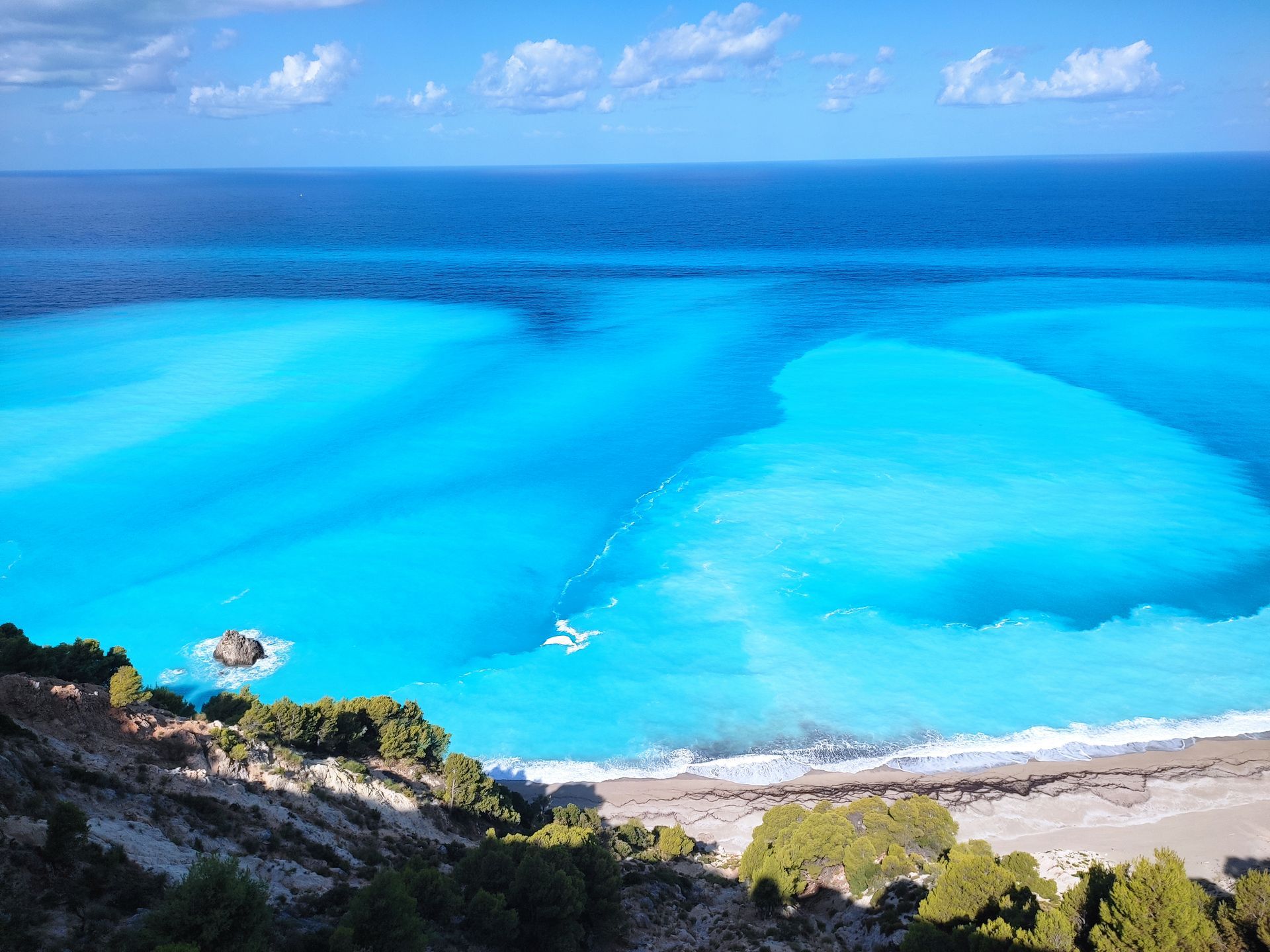 Turquoise tropical bay with sandy beach, green cliffs, and a blue ocean horizon